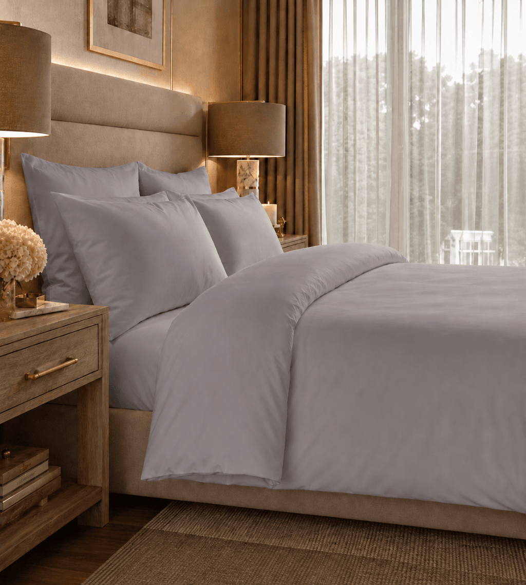 Neatly made bed with gray bedding in a well-lit bedroom.