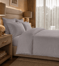 Neatly made bed with gray bedding in a well-lit bedroom.