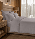 Neatly made bed with gray bedding in a well-lit bedroom.