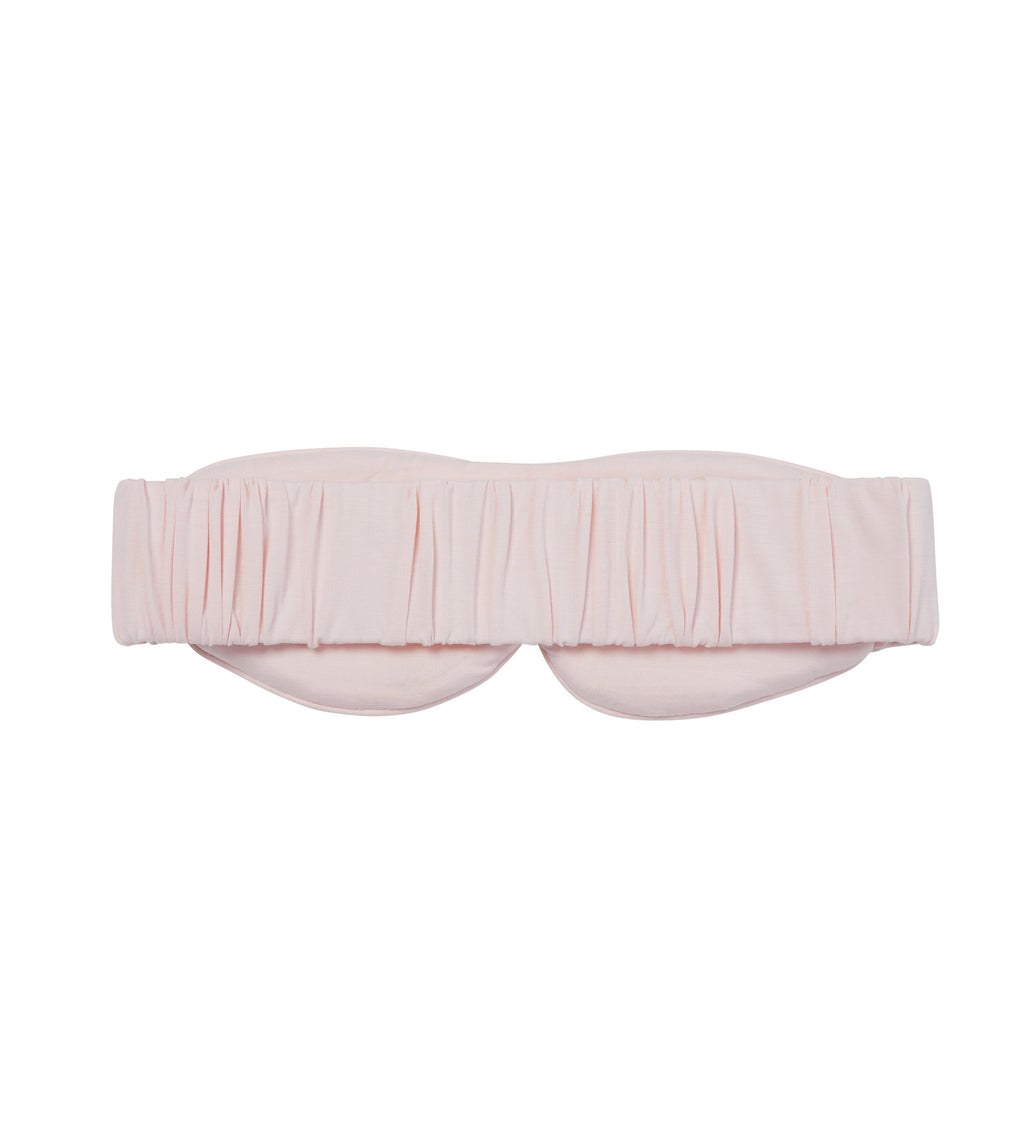 A light pink sleep mask with a gathered, pleated design across the top and a wide elastic strap, shown against a plain white background.