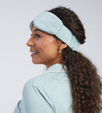 A woman shown in profile wearing a light blue sleep mask against a plain light grey studio background.