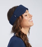 A woman wearing a navy blue sleep mask, shown in profile against a light grey studio background.
