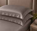 Two dark grey oxford pillowcases stacked on a bed.