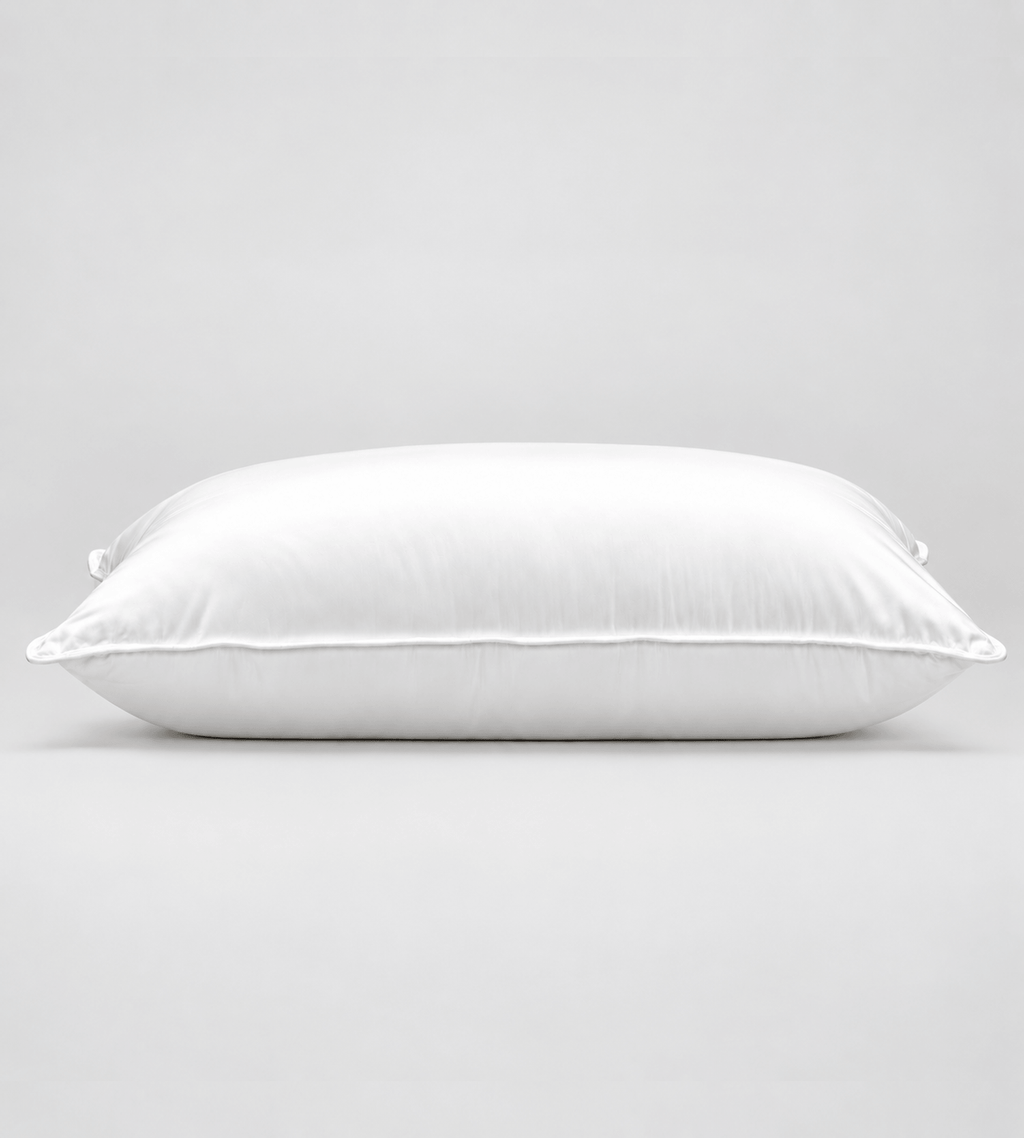 A white rectangular pillow with a smooth, clean surface and piped edges, photographed against a seamless light grey studio background.