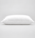 A white rectangular pillow with a smooth, clean surface and piped edges, photographed against a seamless light grey studio background.