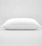 A white rectangular pillow with a smooth, clean surface and piped edges, photographed against a seamless light grey studio background.