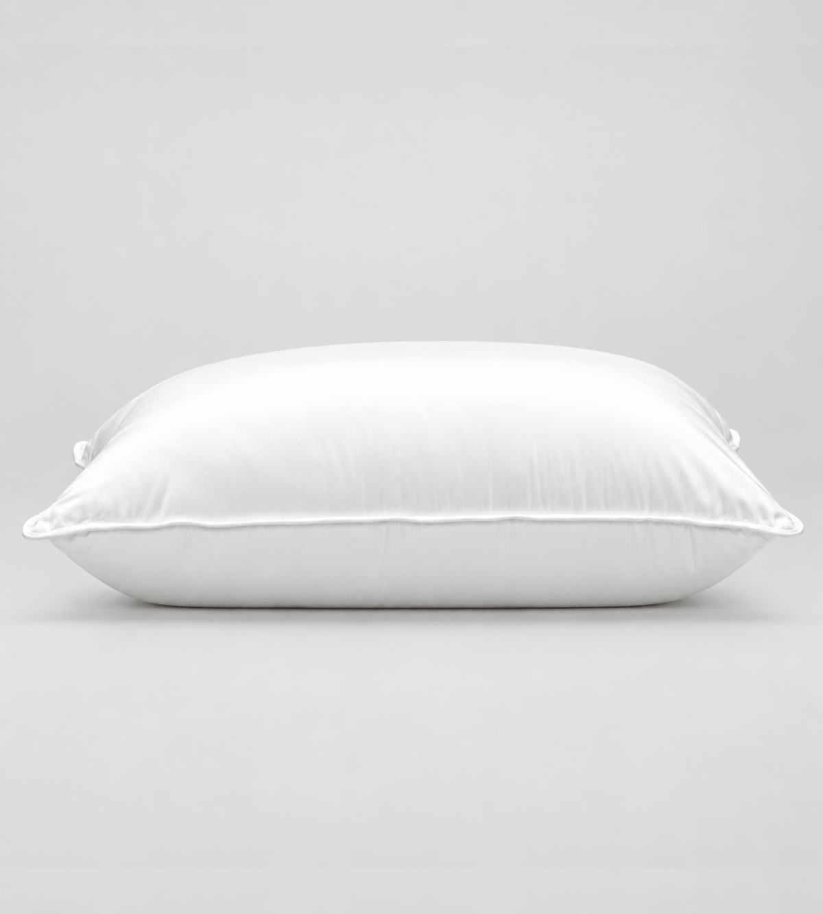 A white rectangular pillow with a smooth satin-like finish, photographed against a neutral light grey background.